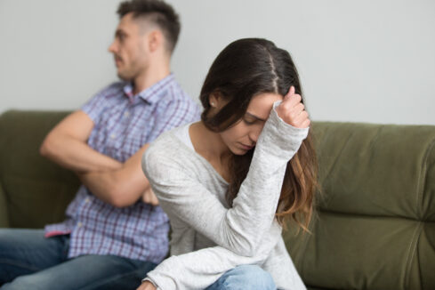 Frustrated woman with stubborn husband in background