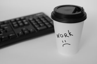 black keyboard next to a to-go coffee cup with a sad face and the word 