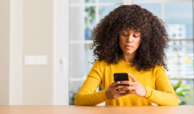 Black woman looking at her phone inside her house