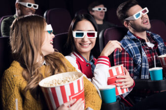 young smiling friends in 3d glasses with popcorn watching movie in cinema