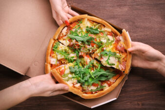 Hands grabbing slices of pizza from a cardboard box