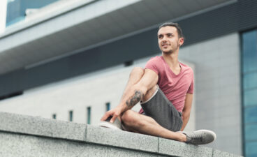 Tattooed man doing yoga asana on street