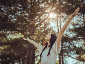 Happy woman standing with her arms open in the forest