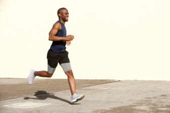 Full body happy young african american man running on street by wall