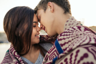 Young couple kissing while wrapped in a blanket together outside