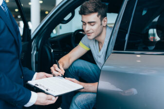 cropped view of car dealer holding clipboard while cheerful man signing contract