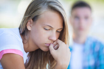 Young girl biting her nails with man in background