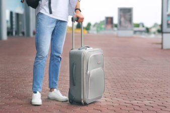 Man with luggage standing at airport parking, waiting for taxi or bus