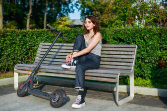 girl lacing up her shoes on a bench next to an electric scooter