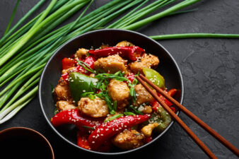 Schezwan Chicken or Dragon Chicken in black bowl at dark slate background. Szechuan Chicken is popular indo-chinese spicy dish with chilli peppers, chicken and vegetables.