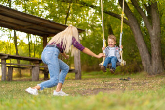 blonde woman pushing a laughing boy on a swing