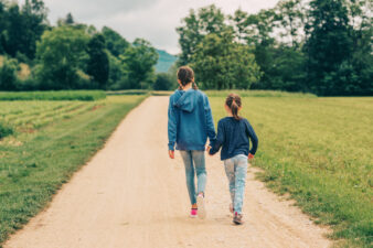 Two little girls walking in fields, happy childhood in countryside, kids spending time in the nature, back view