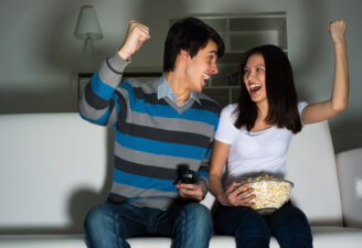 cheering couple watching TV on the couch eating popcorn