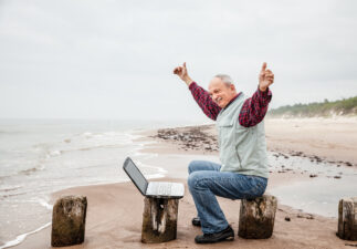 Happy old man with a laptop on the beach on a foggy day