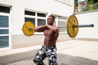 Shirtless man doing squats with a weight