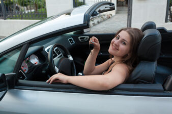 smiling woman sitting in convertible car and holding car keys