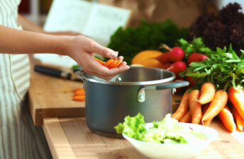 Cropped view of woman putting vegetables into pot