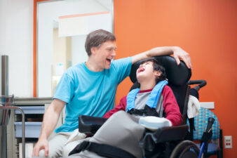 Disabled little boy in wheelchair talking with father in hospital room