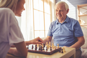 Volunteer and old man playing chess