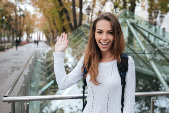 Smiling woman waving and saying hello to you in park