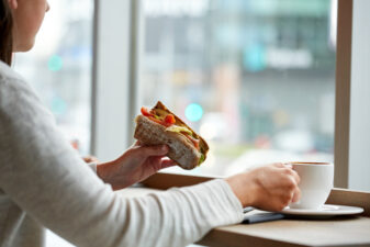 woman eating sandwich and drinking coffee at cafe