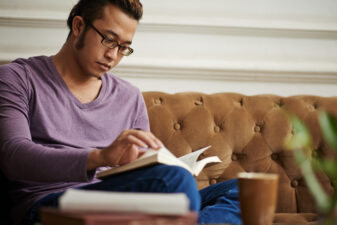 Man in glasses sitting on couch reading book