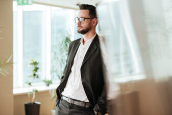 Man in glasses and suit leaning against wall