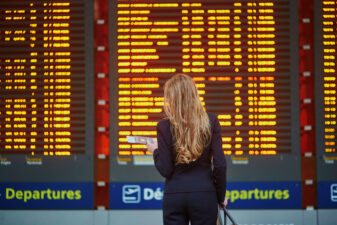 Woman pulling luggage standing in front of flight schedule