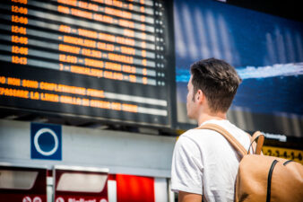 Young man traveling, reading train timetable in railway station