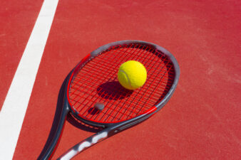 Tennis balls and racket on red court