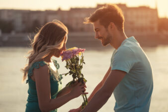 man giving a woman flowers near water