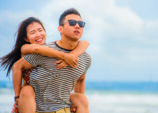 Asian couple giving a piggyback ride on the beach