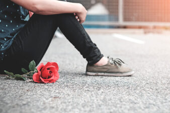 Woman sitting against wall next to red rose