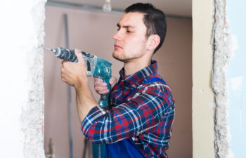 man wearing a plaid shirt using a power drill on the wall