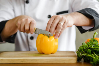 Chef chopping yellow pepper on wood cutting board