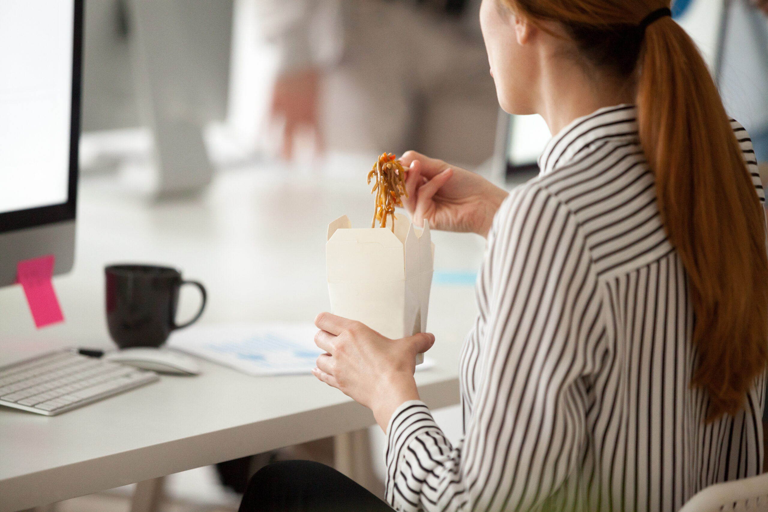 Female employee eating Asian noodles during office work break