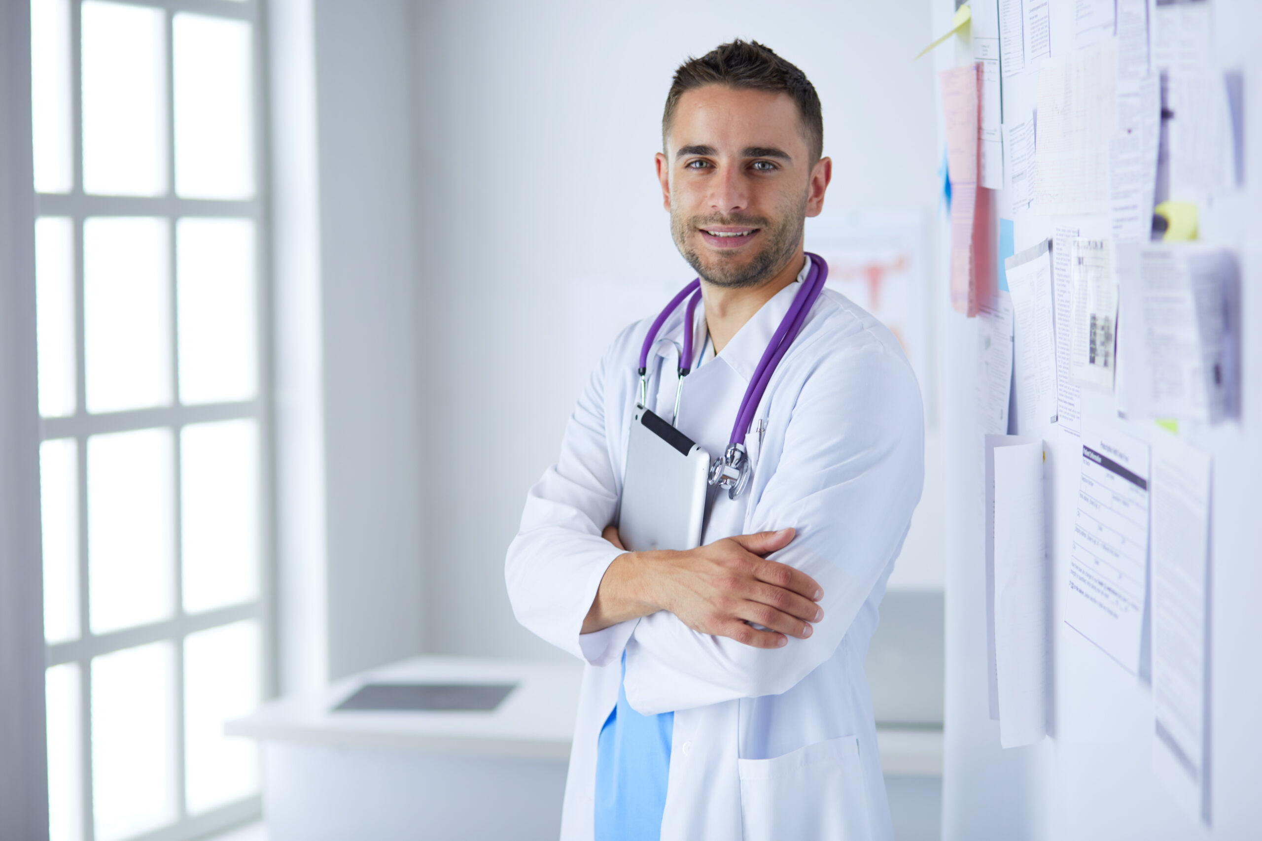 Young and confident male doctor portrait standing in medical office.