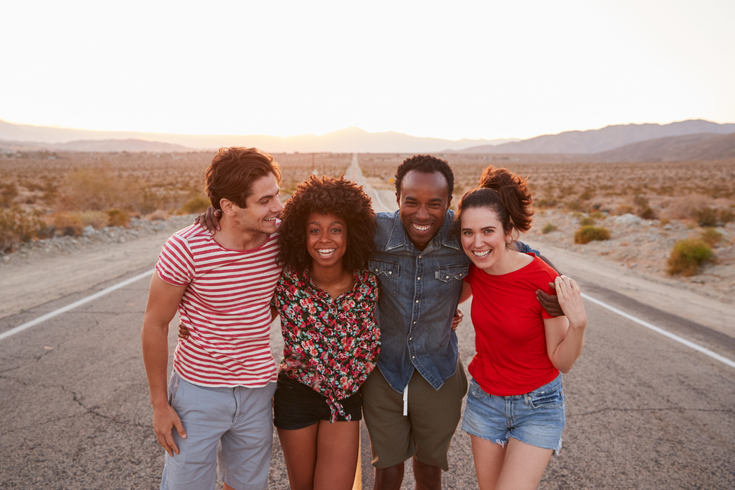 Four happy friends standing on a desert highway, close up