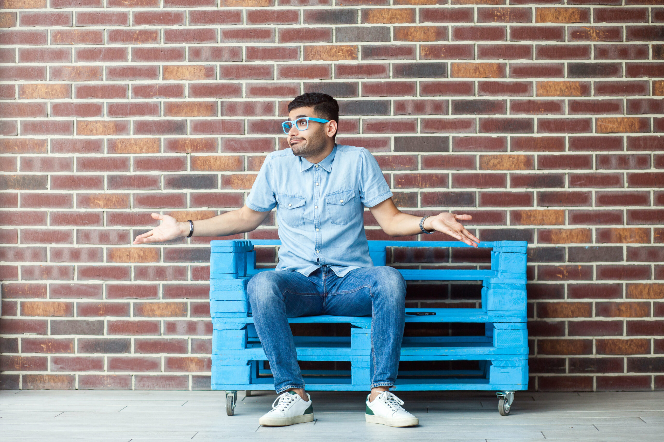 Man sitting on a blue bench shrugging his shoulders