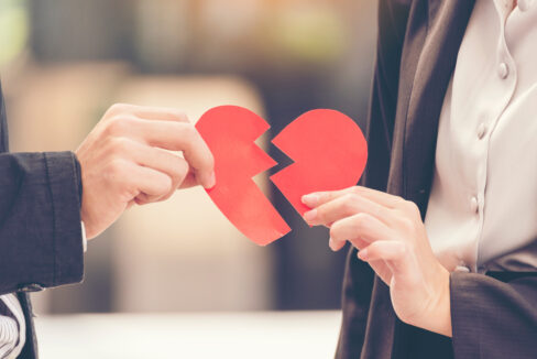 couple each holding one half of a red paper heart