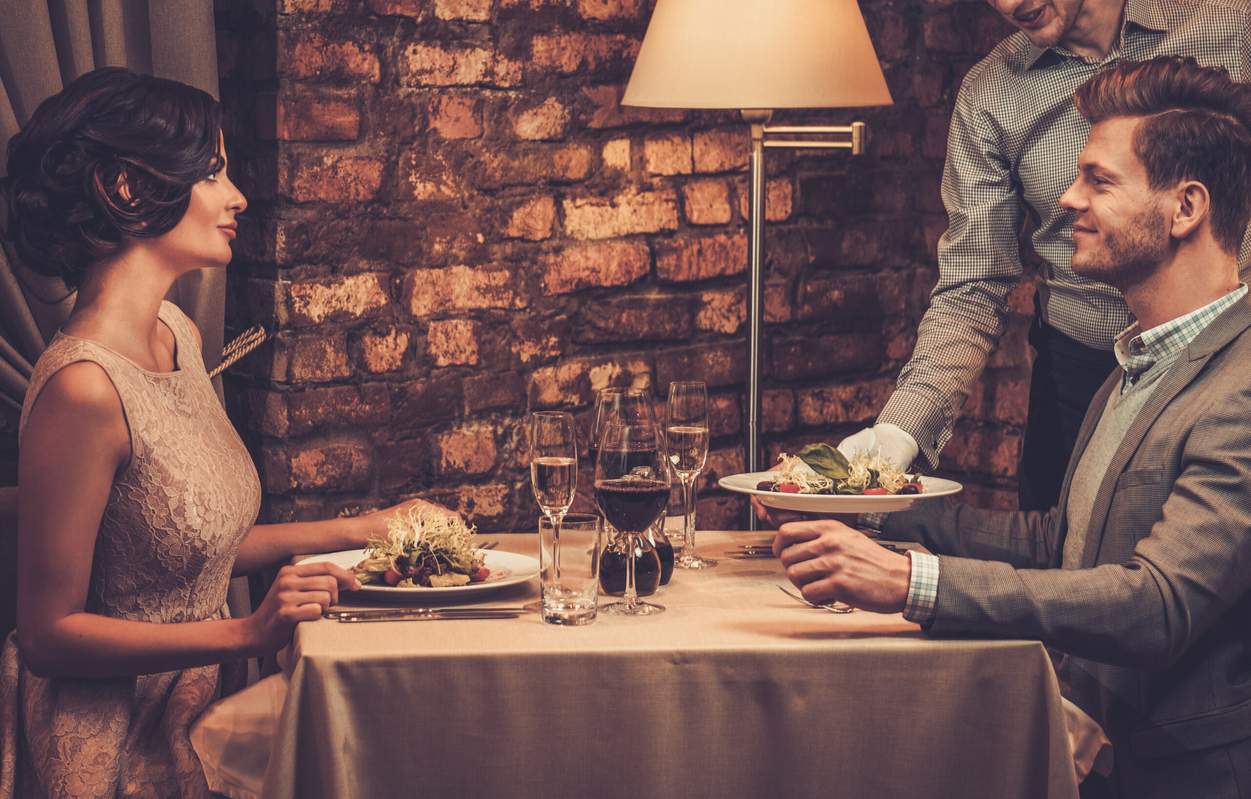 Waiter serving a plate of salad to stylish wealthy couple in a restaurant.