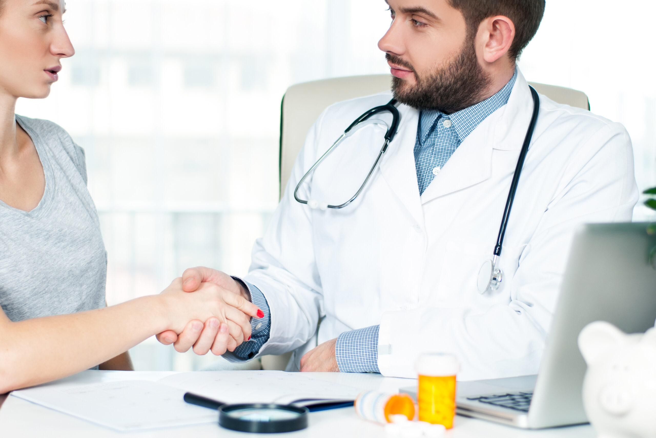 Smiling doctor shaking hands with a female patient in the office