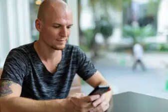 Bald man with tattoo looking at phone