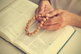 Old man reading the Bible holding onto prayer beads