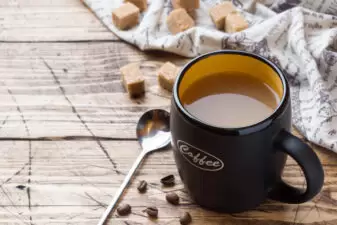 Cup of hot steaming black coffee with sugar cubes on wooden table