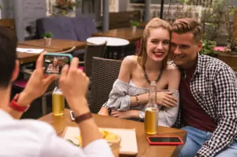 Cute young couple smiling while being photographed by friend