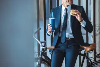 Cropped view of a businessman with a to-go cup and a hamburger