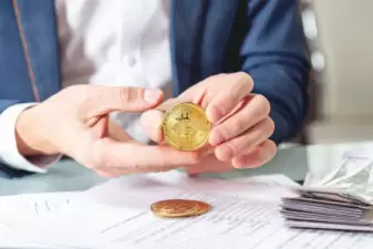 Businessman banker sitting at table with papers holding a coin bitcoin. Exchange and sale of cryptocurrency for dollars