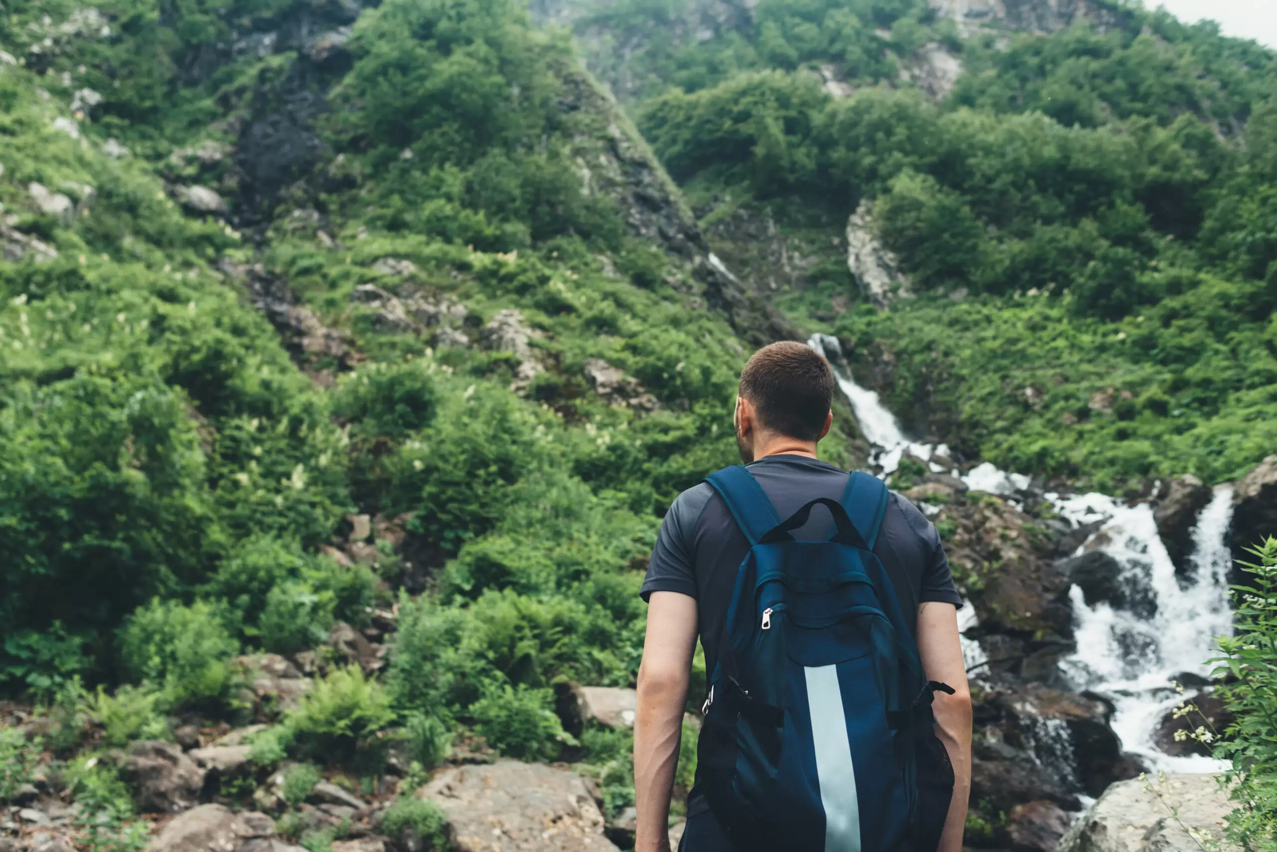 Young man looking at mountain stream in the forest admires nature