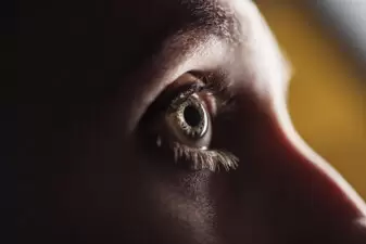 close up view of adult man eye with eyelashes and eyebrow looking away in dark